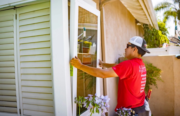 Window installer positioning replacement windows Newport Beach, CA on a residential home exterior.