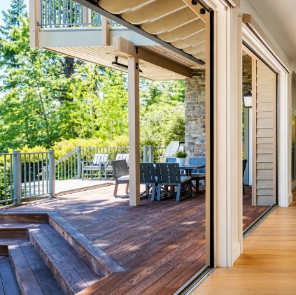 Open bi fold patio doors leading to a wooden outdoor deck with seating area and trees in Costa Mesa, CA.