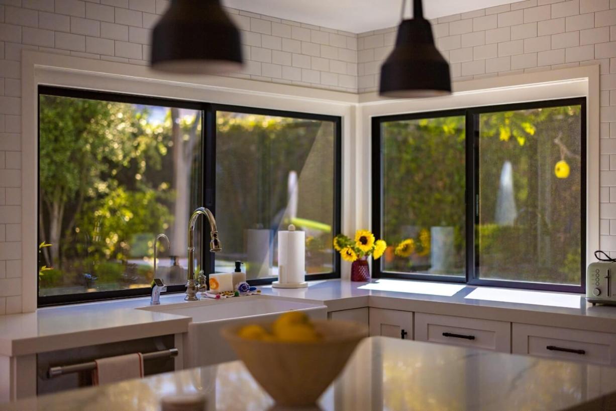 Contemporary kitchen with large black-framed sliding windows above the sink, showcasing Laguna Beach, CA replacement windows that provide expansive outdoor views, natural light, and modern energy-efficient design.